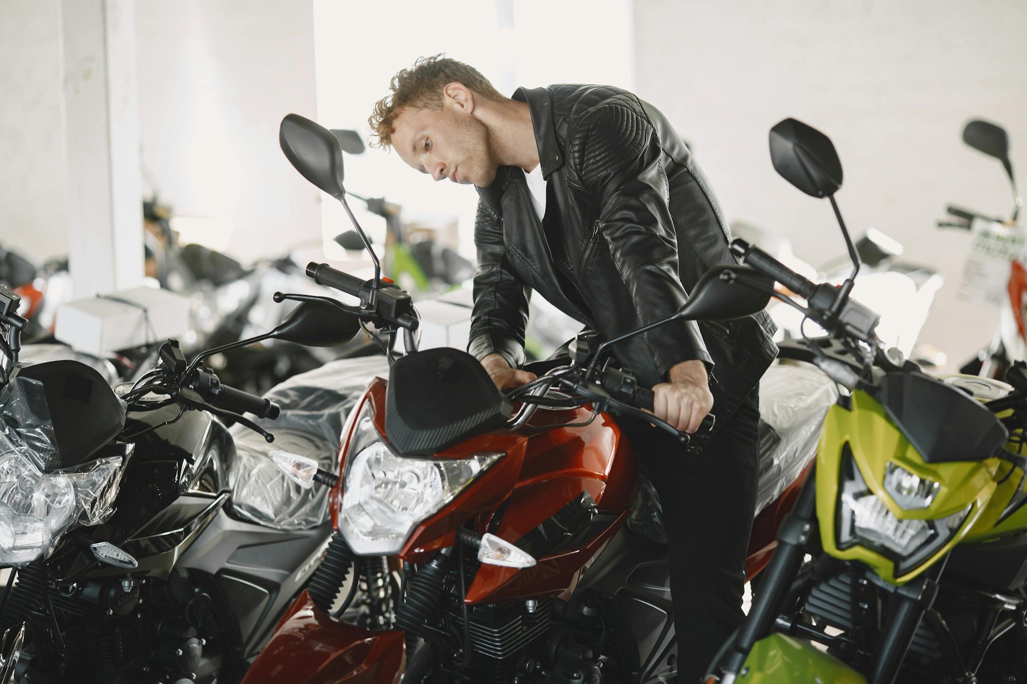 A man in a leather jacket checking motorcycles inside a dealership.
