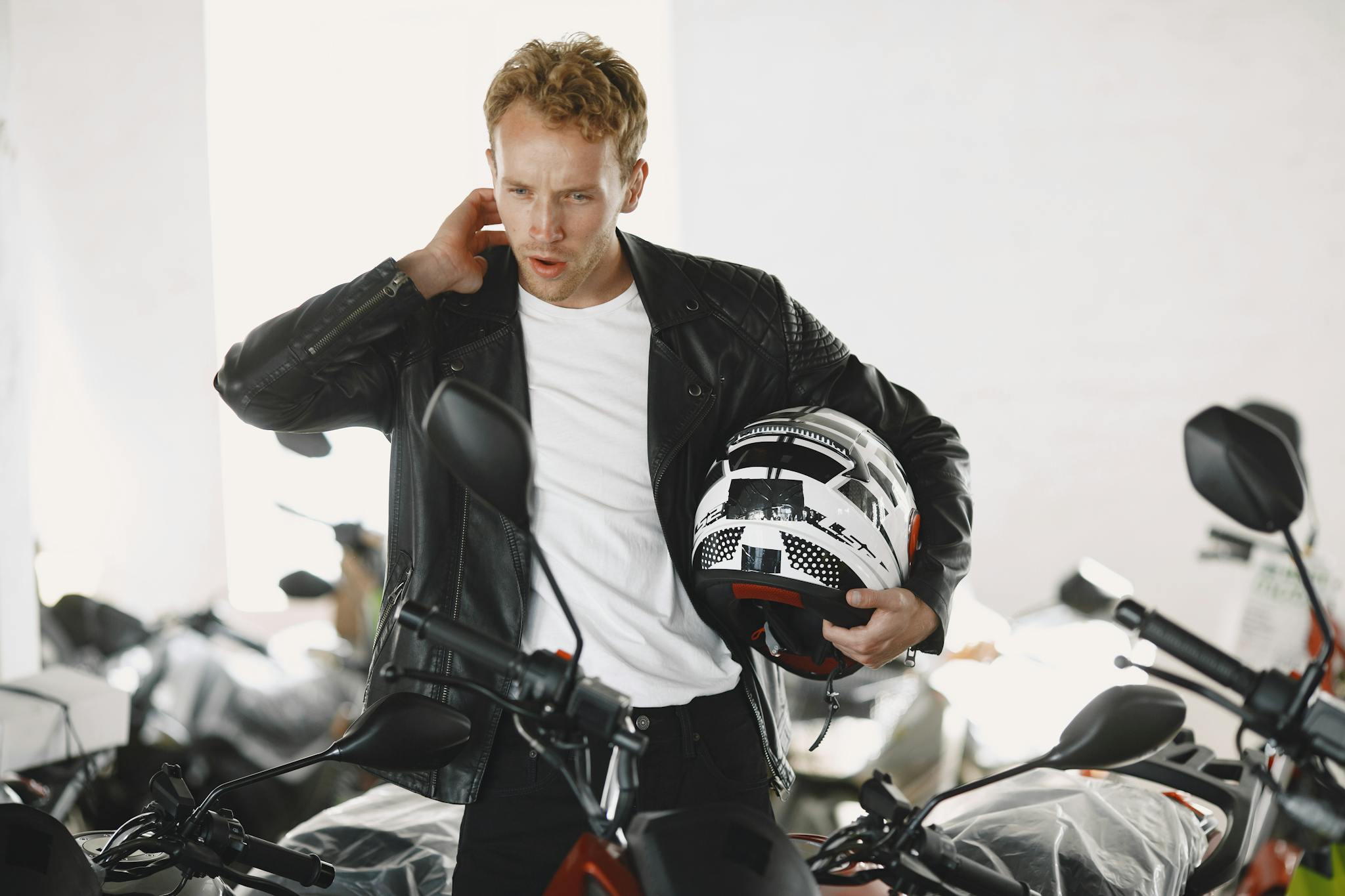 A man in a leather jacket examines a motorcycle in a dealership showroom.